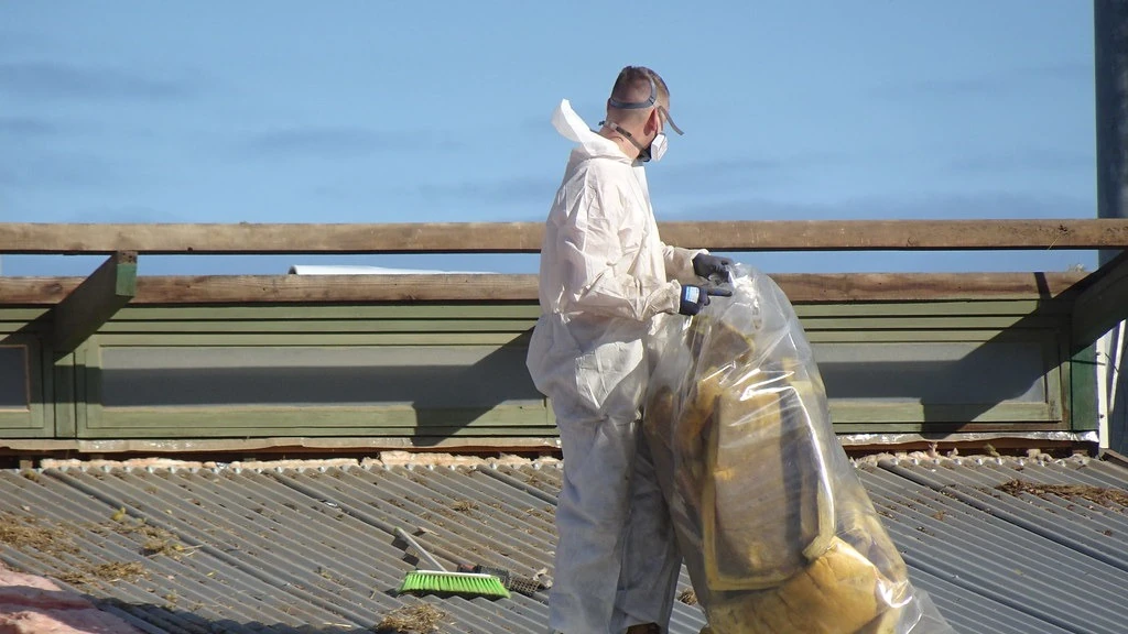 Worker in protective clothing safely bagging removed asbestos roofing material