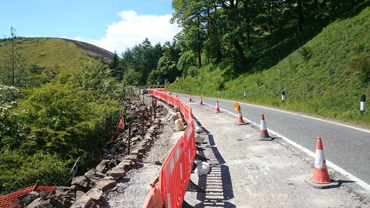 Roadside retaining wall repair showing exposed wall structure and a protected work zone